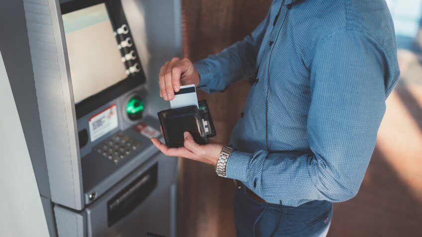 Businessman with suitcase withdrawing money at the ATM.