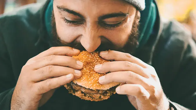 Closeup front view of a mid 20's man biting on a juicy burger outdoors.