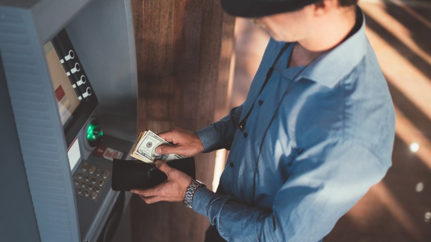 Man at the ATM withdrawing us paper currency and putting in wallet.