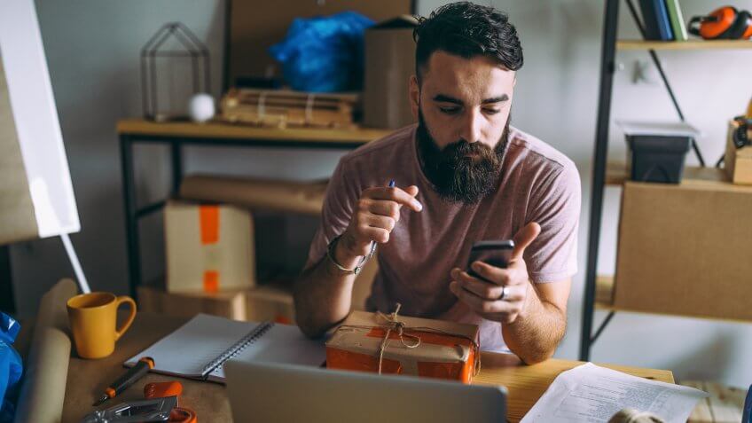 Photo of young man using app for smart phone tracking delivery package in his office.