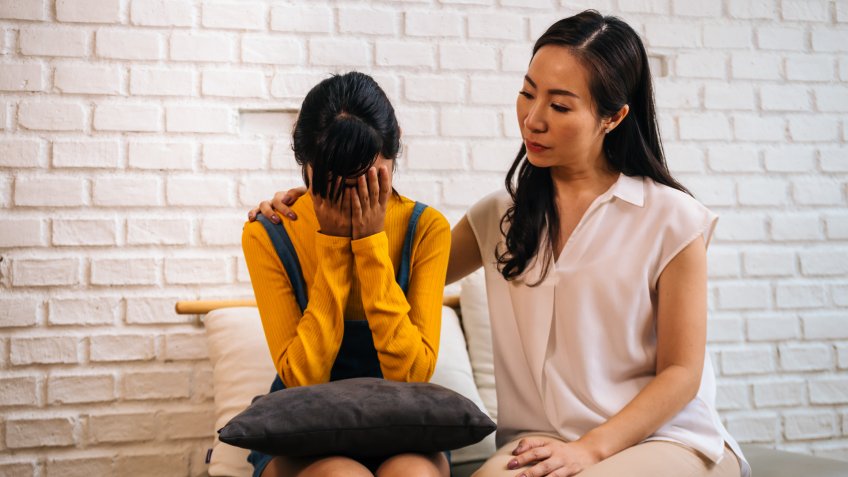 Asian mother comforting crying teenage daughter in miserable, stressed, depressed, sad state of mind.