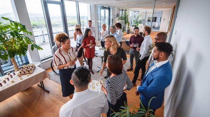 High angle view of diverse group of business professionals enjoying appetizers and sparkling wine at new business launch party.