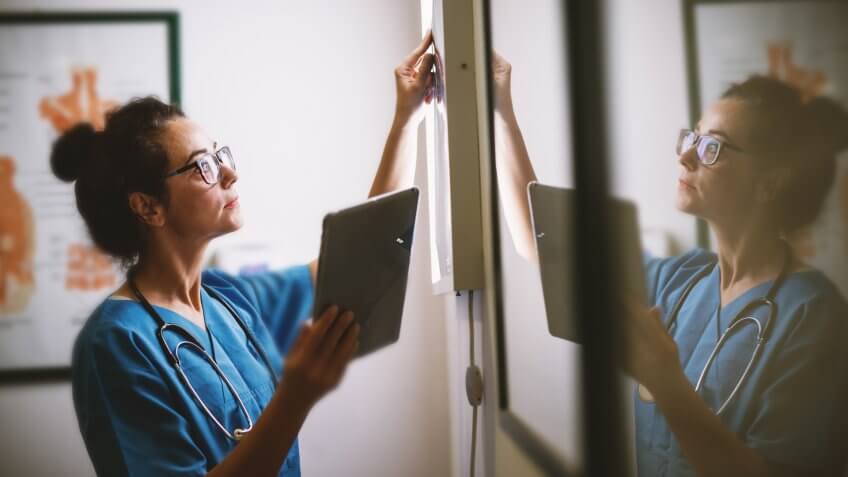 Side view of smiling middle aged nurse checking X-ray in a doctors office.