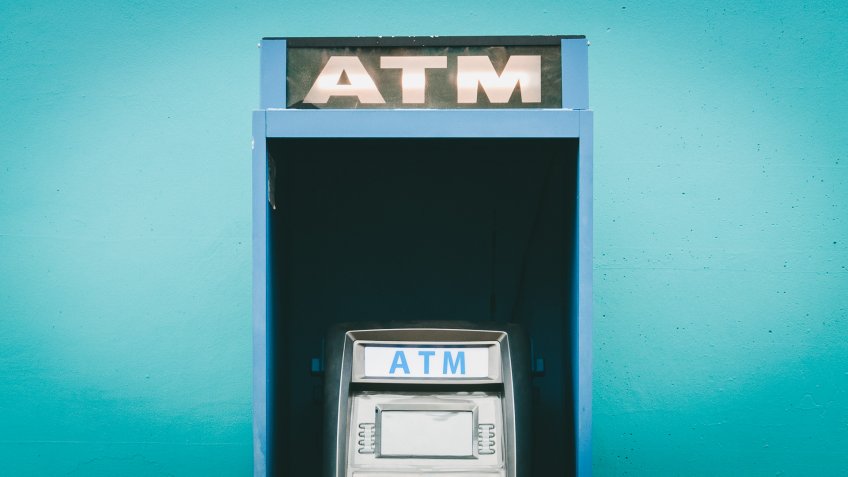 blue public ATM, Automated Teller Machine on street in front of wall.