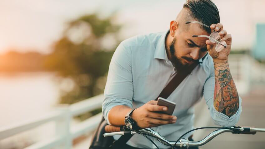 Businessman pushing his city bicycle and using his smart phone.