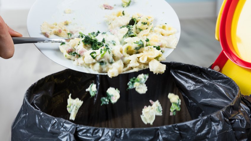 Close-up Of A Person Throwing The Leftover Pasta Into The Trash Bin.