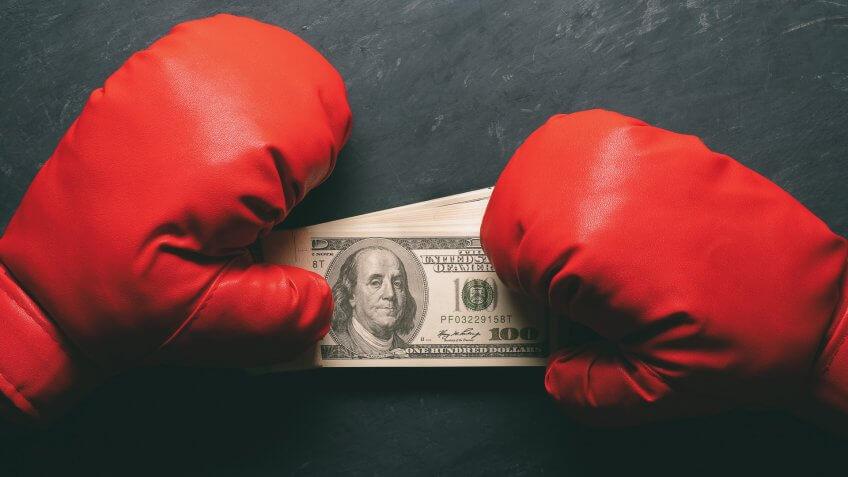 Boxing Gloves holds the dollar banknote on black cement background.