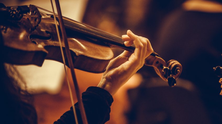 Close up shot of a woman performing on a violin during a concert.
