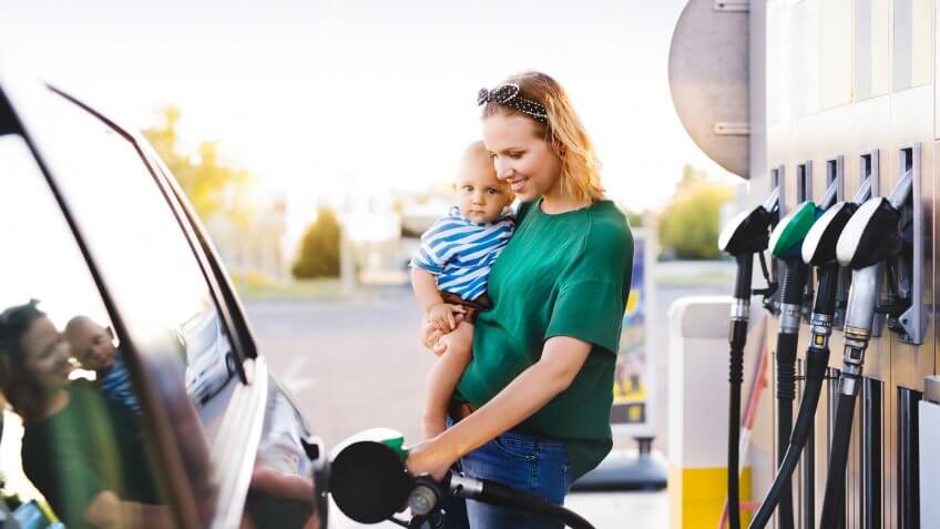 Young mother with baby boy at the petrol station refuelling the car.