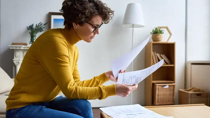 Concentrated woman reviewing financial documents at home.