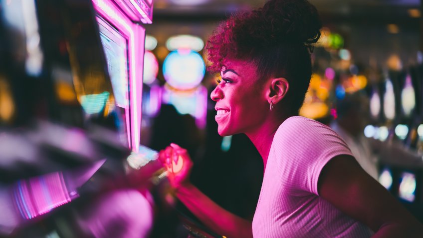 woman having fun playing slot machine at casino pulling lever.