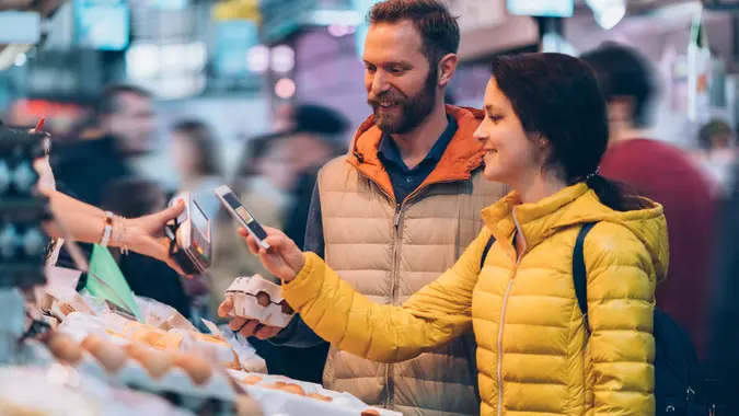 Smiling couple buying fresh eggs and paying contactless with smartphone.