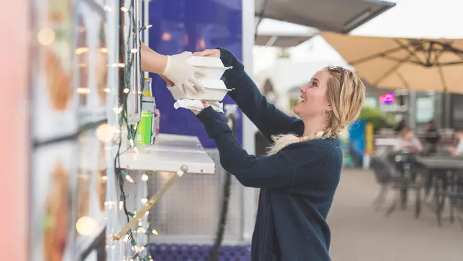 Cute woman in her early 20s orders lunch at an outdoor food cart.