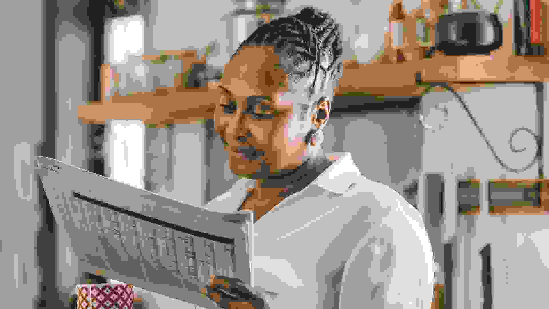 Smiling African American woman drinking a cup of coffee and reading the newspaper while standing in her kitchen in the morning.