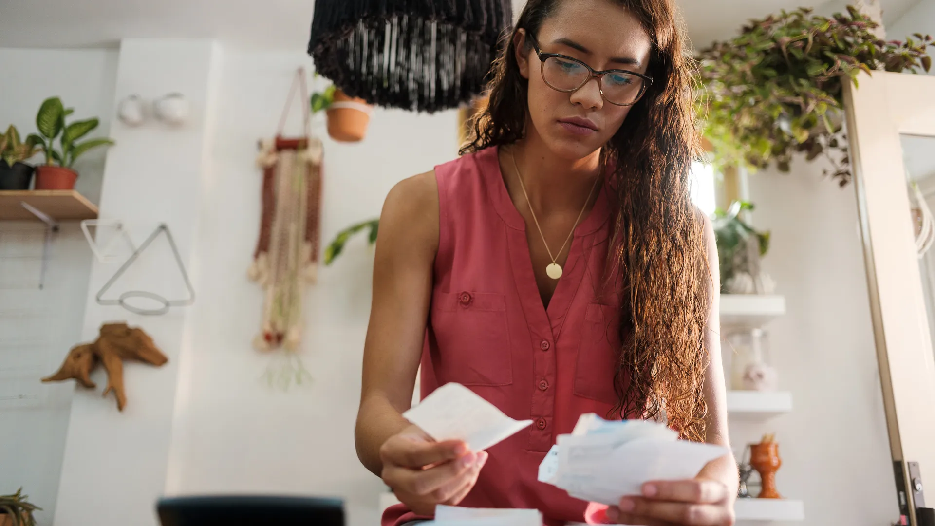A young latin woman sitting, holding receipts and looking at them with a worried face.