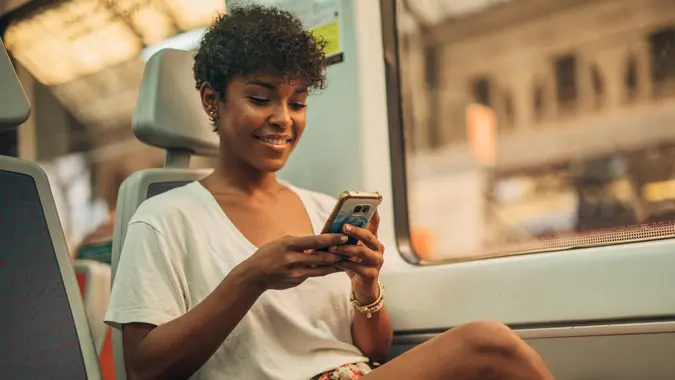 One woman, beautiful young lady riding in train, using mobile phone.