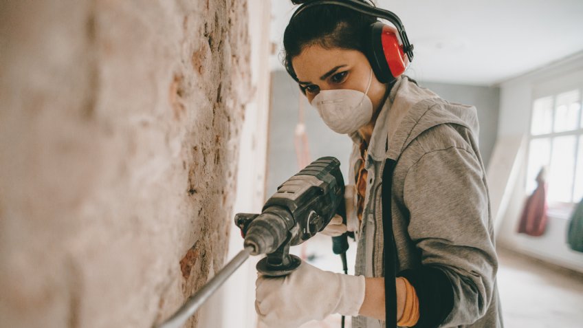 Young woman using drilling machine during reconstruction of her apartment.