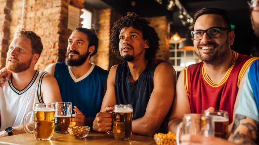 Multi - ethnic group of basketball fans watching a basketball game and drinking beer at the pub.