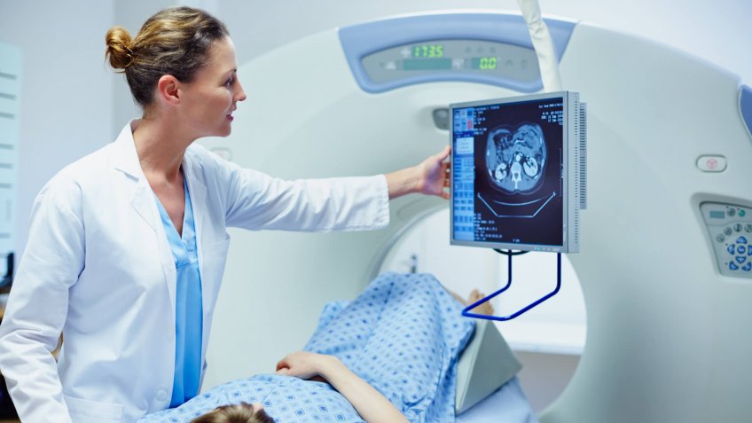 Female doctor showing CT scan to patient in examination room at hospital.