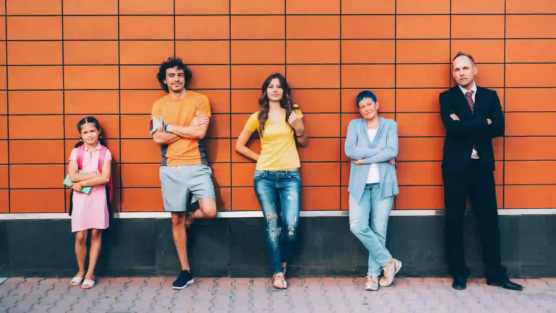 Five people at different ages standing agains a wall seperately.