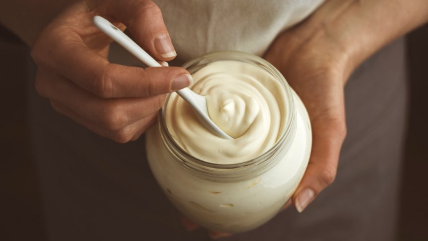 Glass jar of mayonnaise and a white spoon in hand.