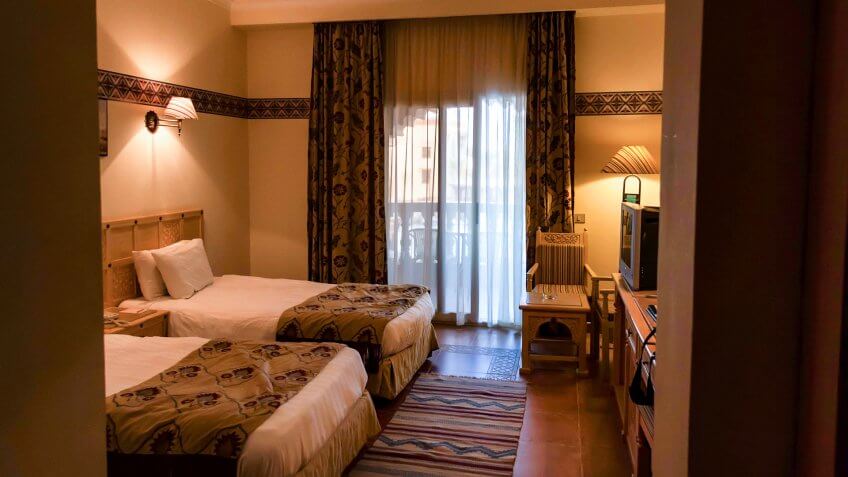 Two neatly done beds in hotel room in beige tones.