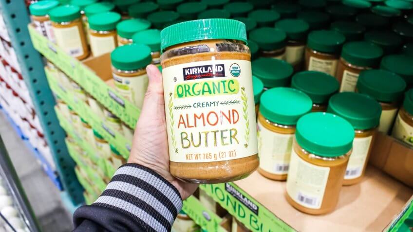 Tustin, California/United States - 02/08/2020: A hand holds a jar of Kirkland Signature organic creamy almond butter on display at a local Costco.
