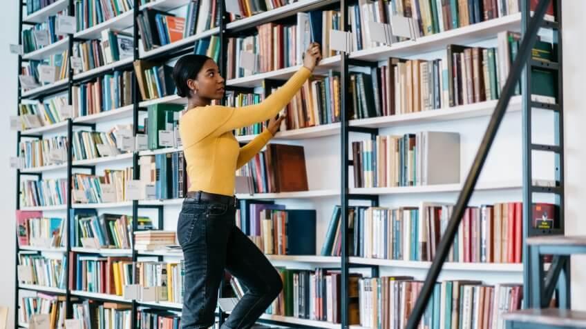 African american female librarian dressed in casual wear choosing literature book for exam preparation.