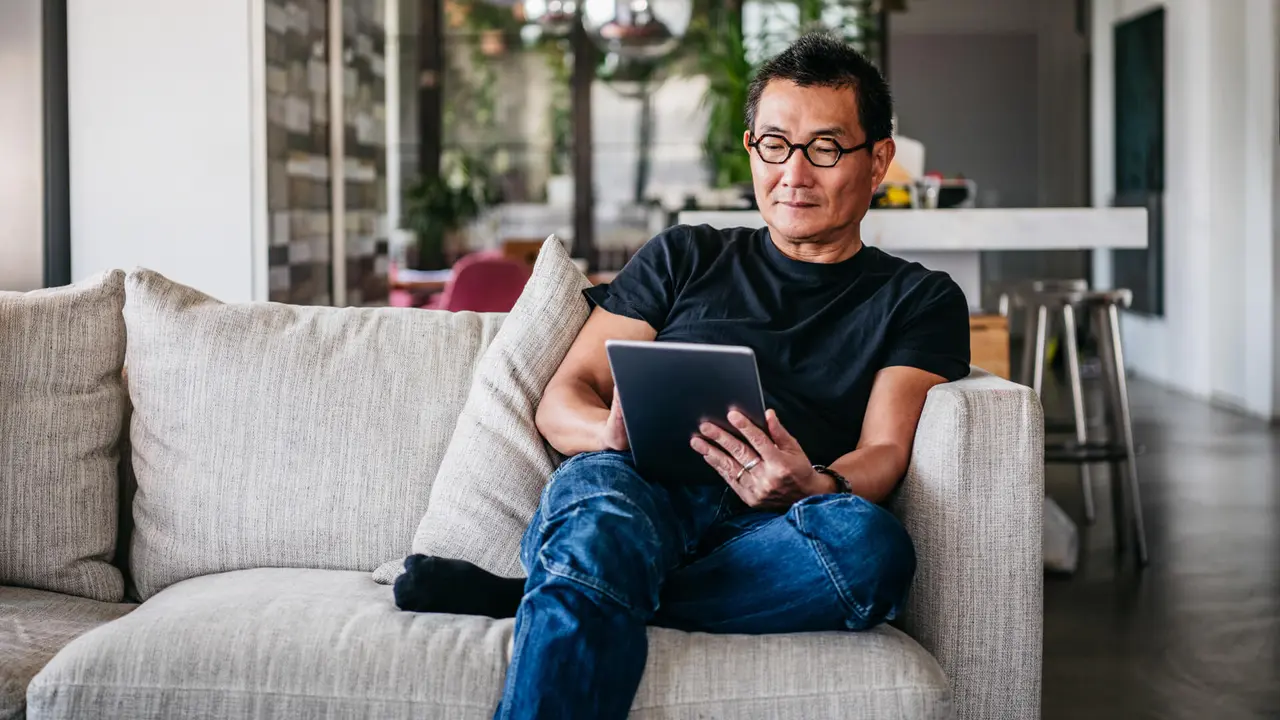 Chinese man in his 50s relaxing at home on sofa, casual clothes, reading ebook, surfing the internet.