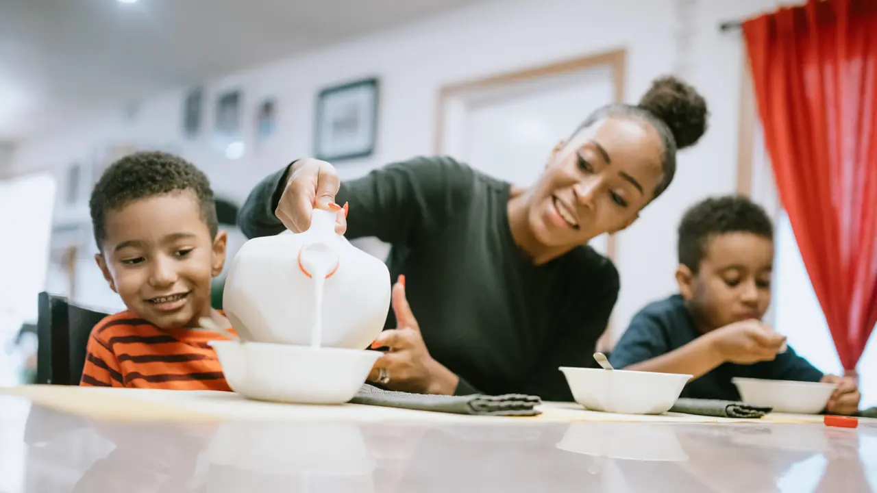 A mom sits at a table eating cereal with her sons at home.