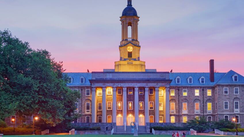 Students chat in front of Old Main, the main administrative building of Penn State after sunset.