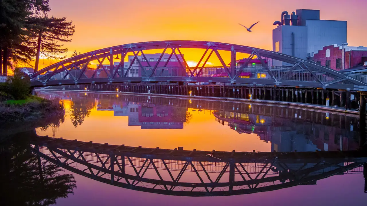The hues of the rising sun are reflected in the mirror-like surface of the Petaluma River turning basin along the historic Petaluma, California, downtown waterfront.
