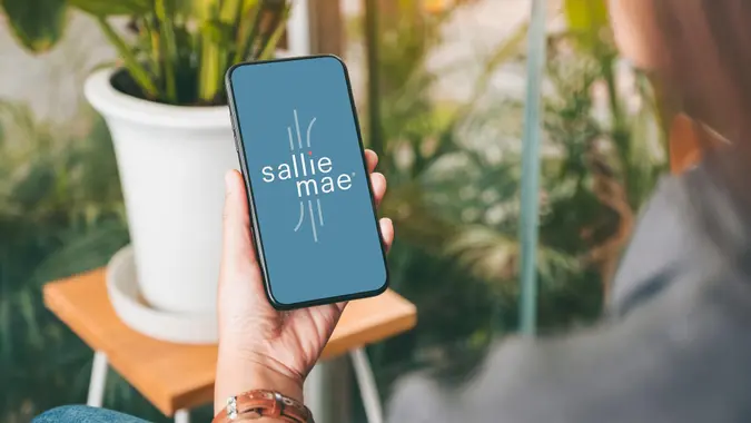 Woman outside by her plants holding phone in left hand while using the Sallie Mae mobile app.