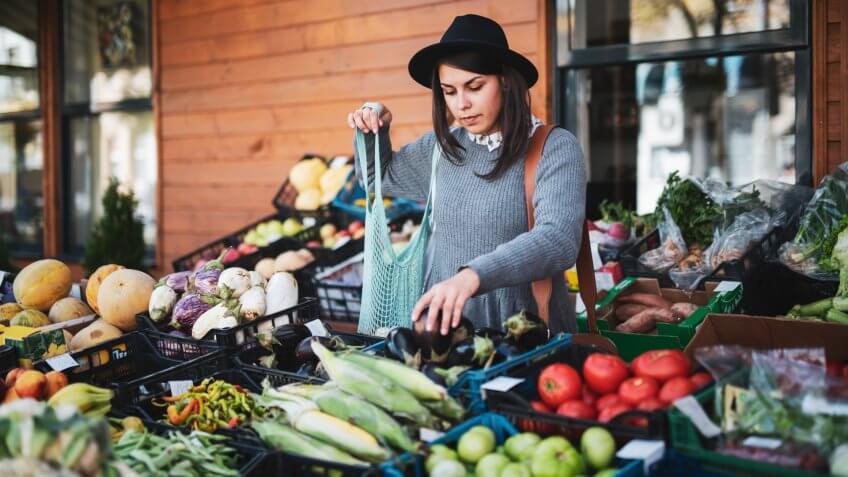 Young woman buying fruit and vegetables at outside market, she choosing eggplant.