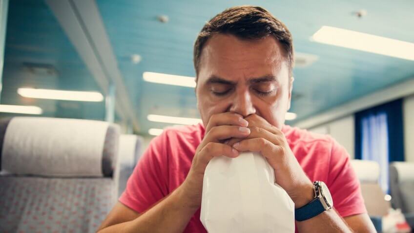 Nauseous man holding a bag to his mouth, hyperventilating.