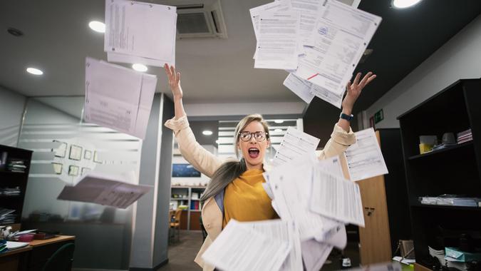 Stressed woman throws papers in the office in an image of relief.