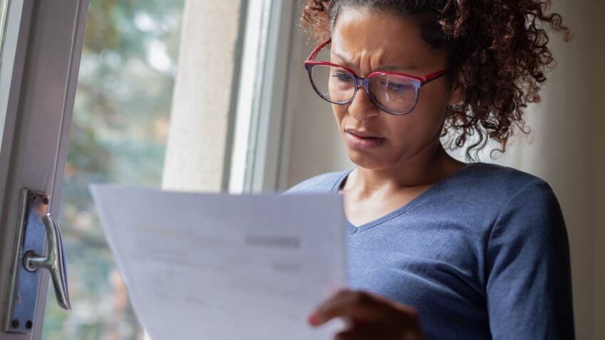 Sad black woman near window reading bad news letter.