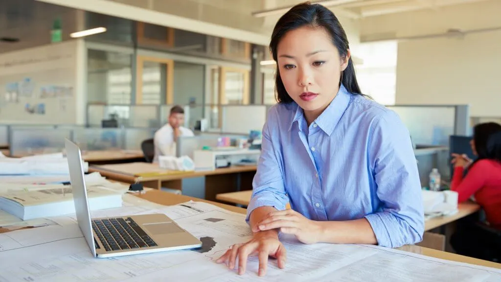 Female Asian architect studying planes in open plan office.