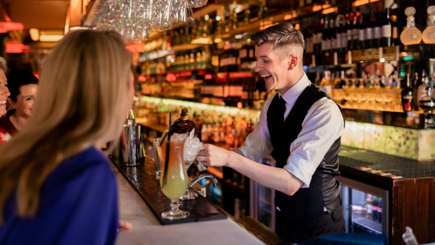 Young bartender making a cocktail for a small group of women enjoying ladies night.