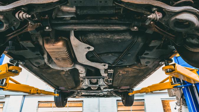 View of car undercarriage when lifted on hydraulic lift in a workshop during inspection.