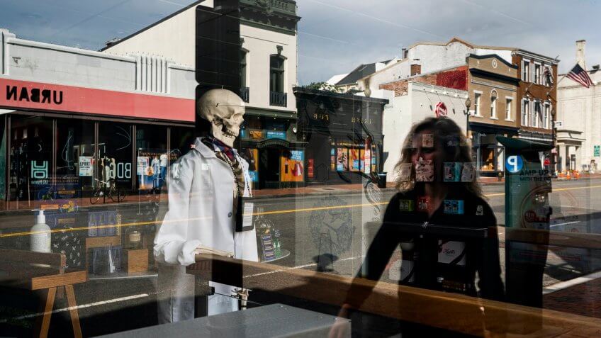 A woman is reflected in a shop window with a skeleton on display at a normally busy M Street in Georgetown is near empty before lunch hour in Washington, DC, USA, 27 March 2020.