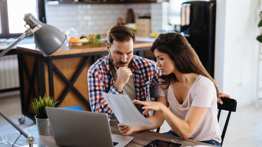 Frustrated couple checking bills at home using laptop.