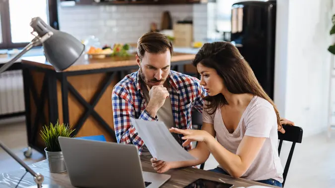 Frustrated couple checking bills at home using laptop.