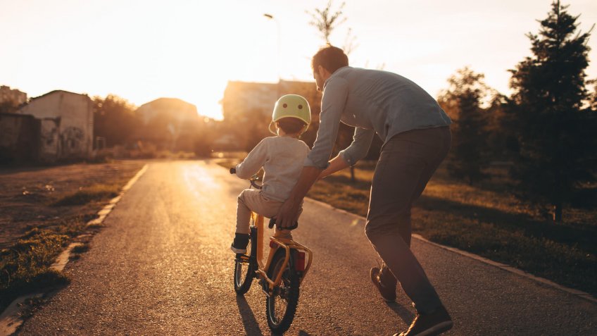 Photo of a young boy and his father on a bicycle lane, learning to ride a bike.