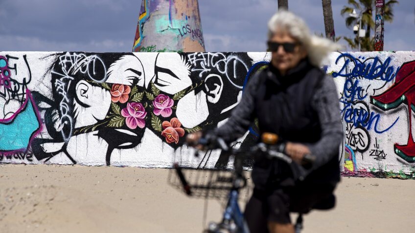 A woman rides her bike past a mural showing a couple kissing with face masks next to the beach amid the coronavirus pandemic in Venice, California, USA, 28 March 2020.