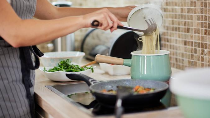 Woman preparing dinner. Caucasian woman in apron standing next to stove and preparing spaghetti.