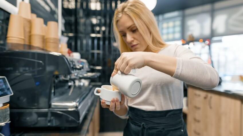 Coffee art, close-up of young beautiful female barista holding milk for prepare cup of coffee.