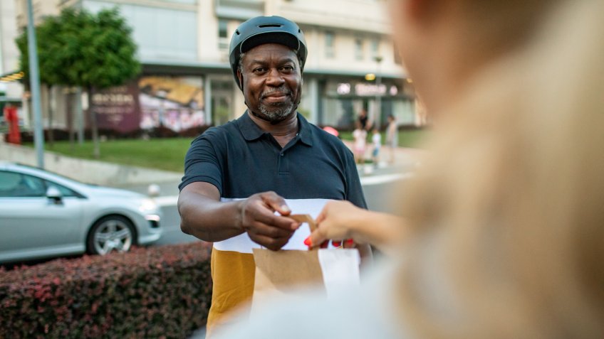 Senior African delivery man delivering bags with food to customer.