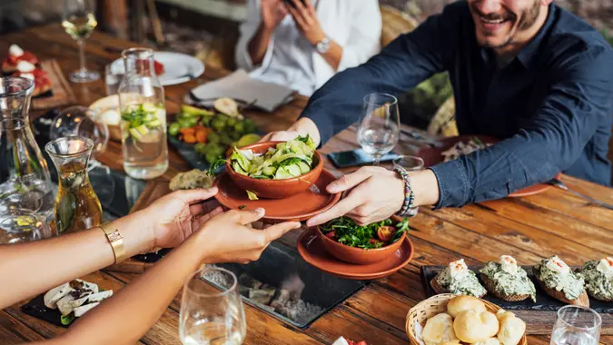 Hands of cropped unrecognisable woman and man passing salad bowl at vegetarian restaurant.