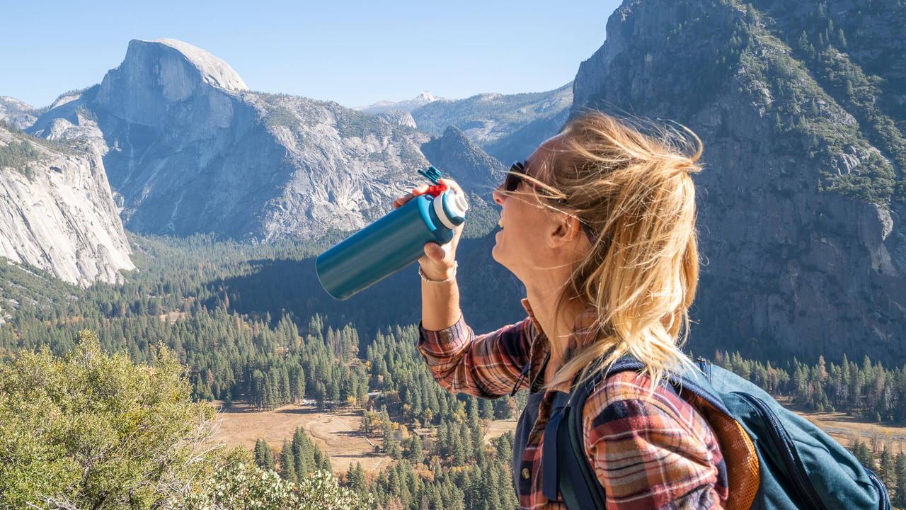 Young woman on top of Yosemite valley, USA drinking water from reusable bottle.
